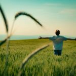 A person with outstretched arms in a lush green field under a clear blue sky in Bursa, Türkiye.